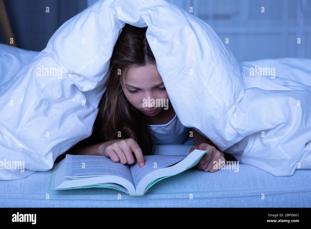 Girl Lying Under White Blanket Reading Book At Night Stock Photo Alamy