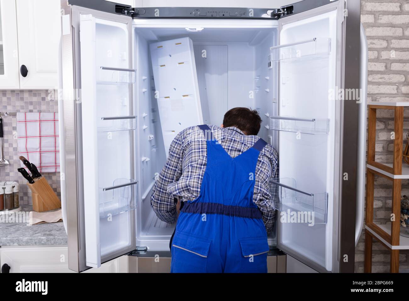 Young Serviceman Checking Fridge With Digital Multimeter Stock Photo