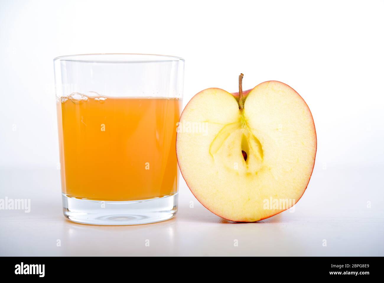 half apple with glass of naturally cloudy juice in front of white ...