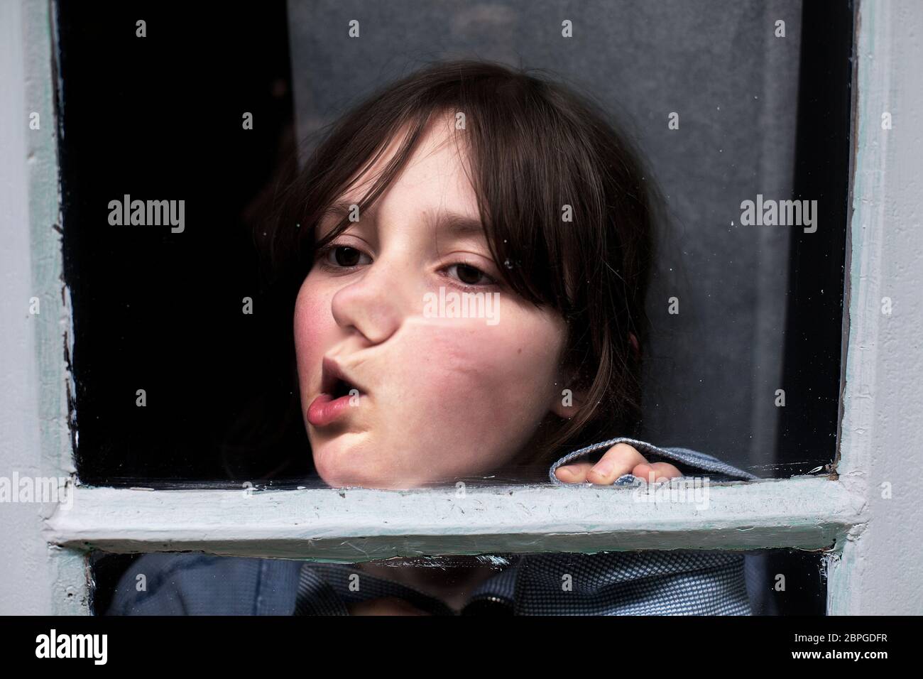 11 year-old boy making against the window pane during lockdown. Stock Photo