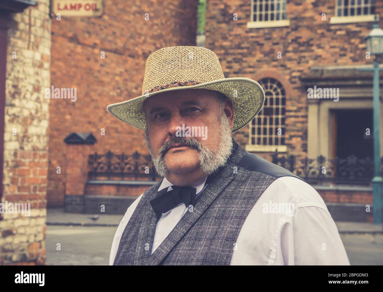 Retro, close-up portrait of smartly-dressed man with moustache in straw hat, isolated outdoors in vintage street at Black Country Living Museum, UK. Stock Photo