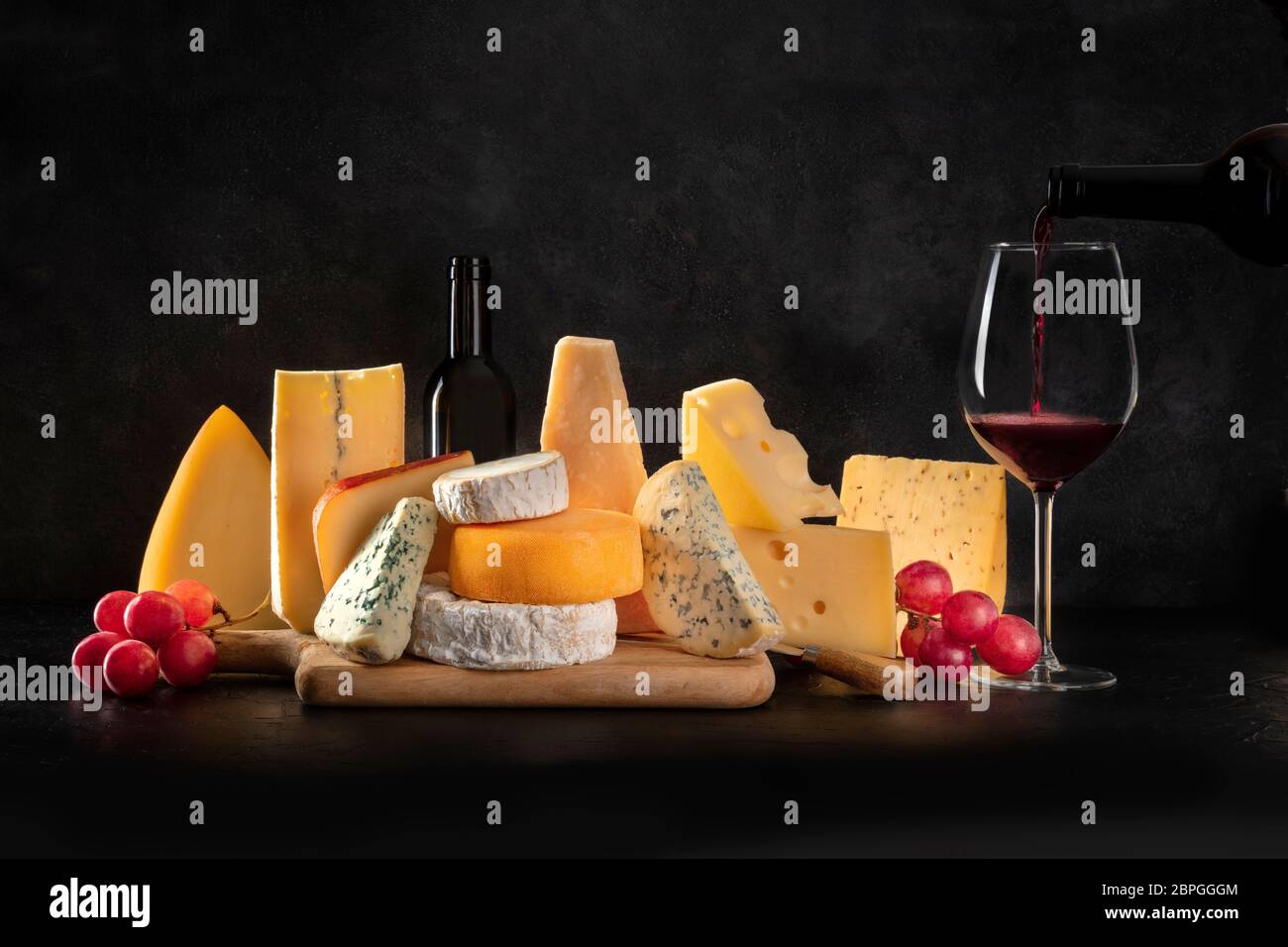 Cheese, many different types with grapes and pouring wine, side view on a black background with a place for text Stock Photo
