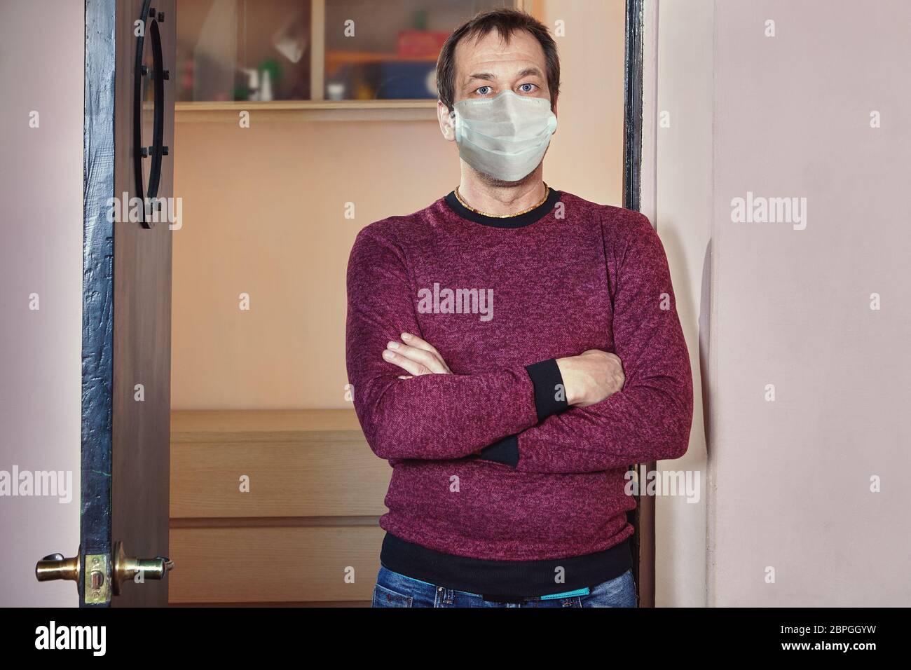 Caucasian white man about 50 years old is standing in his flat in disposable medical facial mask in a period of covid-19 pandemic during home isolatio Stock Photo