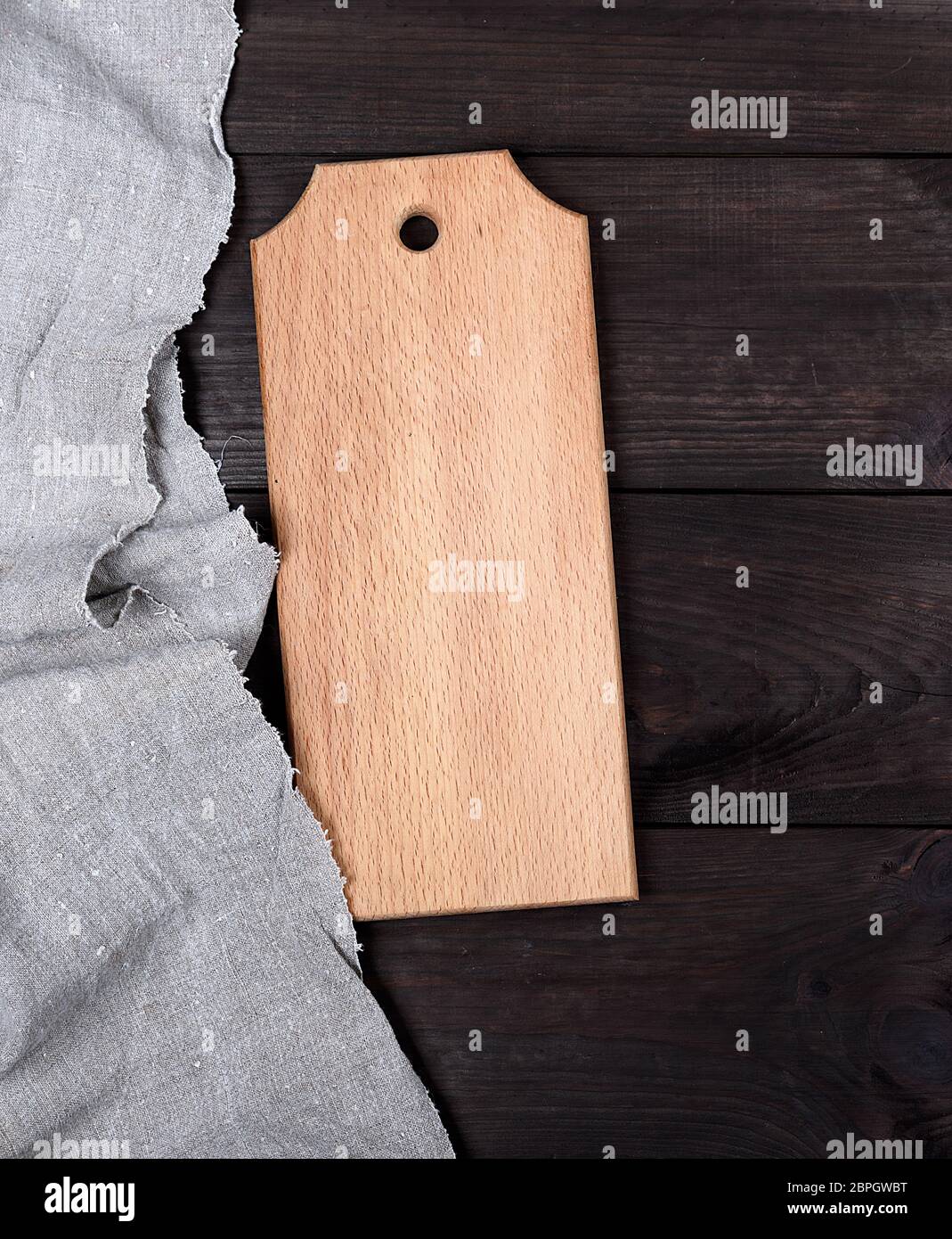 rectangular empty wooden cutting board on a gray linen napkin, brown table Stock Photo