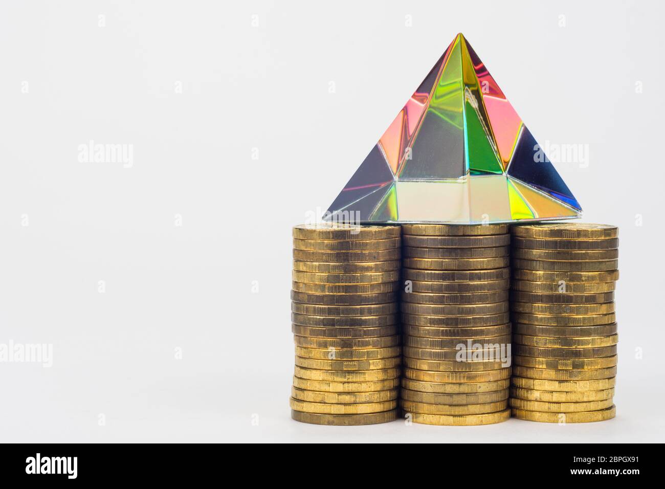 Three piles of coins, there is a glass pyramid on them, to the right is an empty space Stock Photo