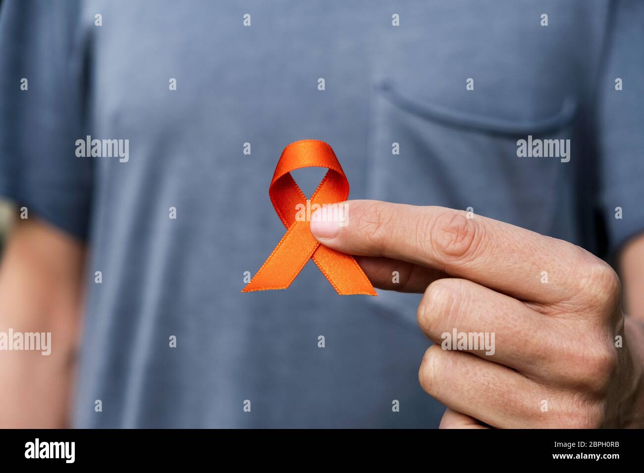 closeup of a young caucasian man with an orange ribbon in his hand, in support of people affected by multiple sclerosis Stock Photo