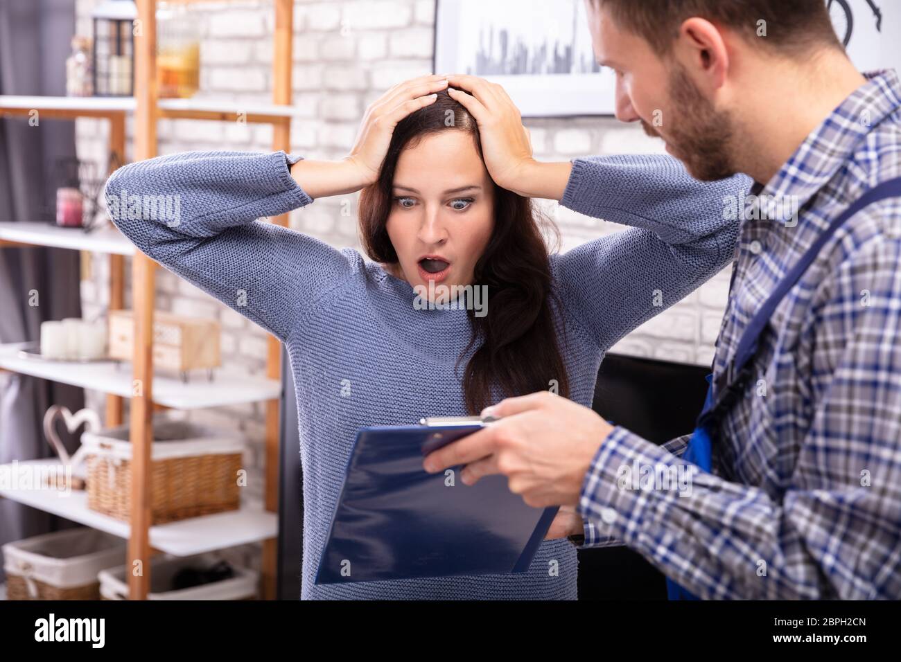 Shocked Woman Looking At Invoice Shown By Male Technician Stock Photo
