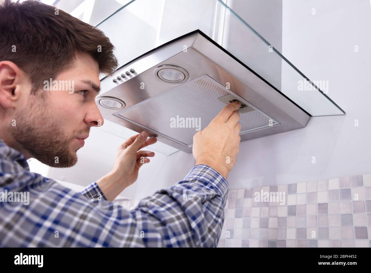 Side View Of Young Male Fixing Kitchen Extractor Filter In Kitchen Room ...