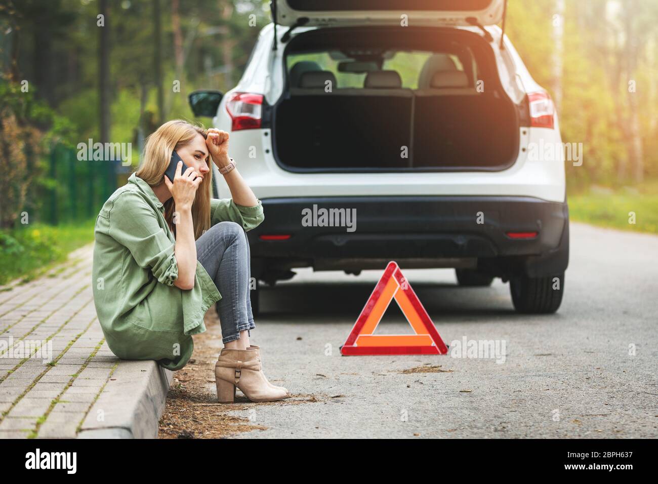 woman is sitting on the side of the road and calling for help because car accident Stock Photo