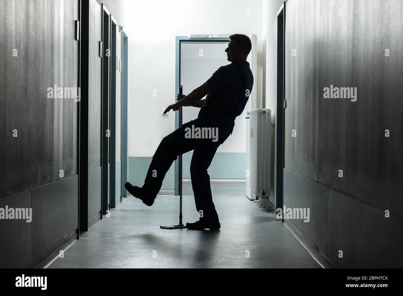 Silhouette Of A Mature Man Falling While Mopping Floor In The Corridor Stock Photo