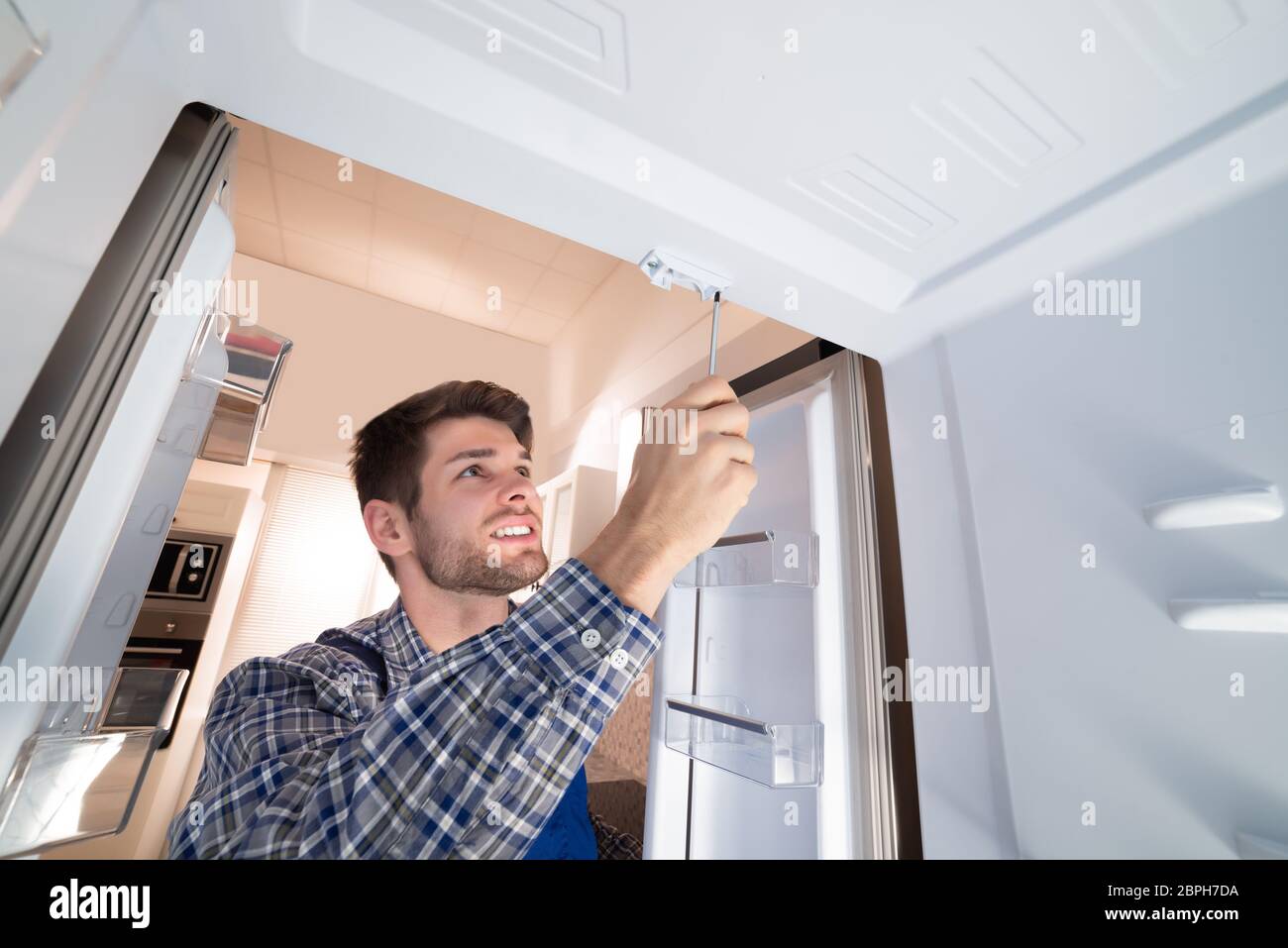 Young Male Technician Checking Refrigerator With Screwdriver Stock Photo