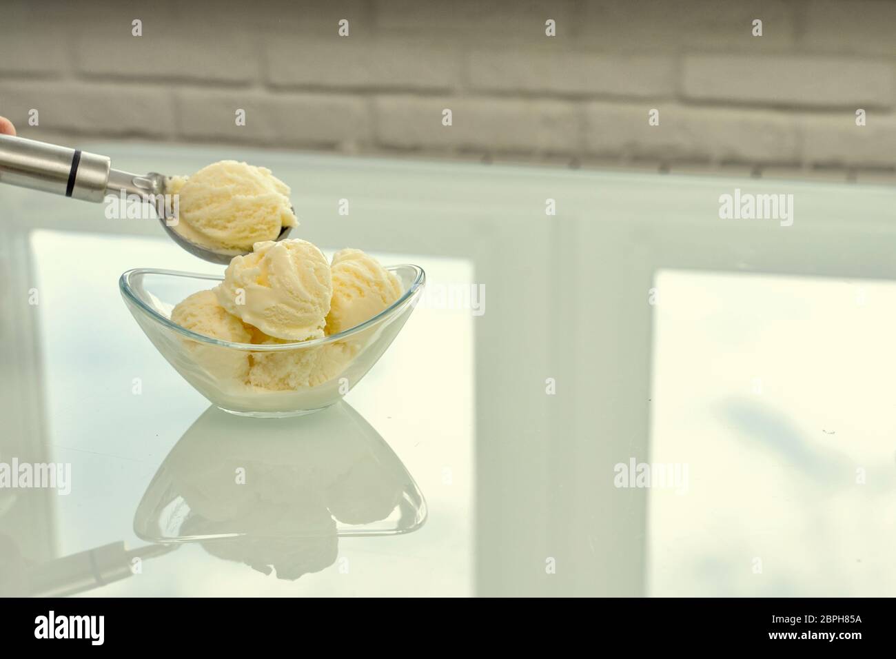 a bowl with vanilla ice cream stands on a reflective bright table. with a metal spoon report another 1 ball Stock Photo
