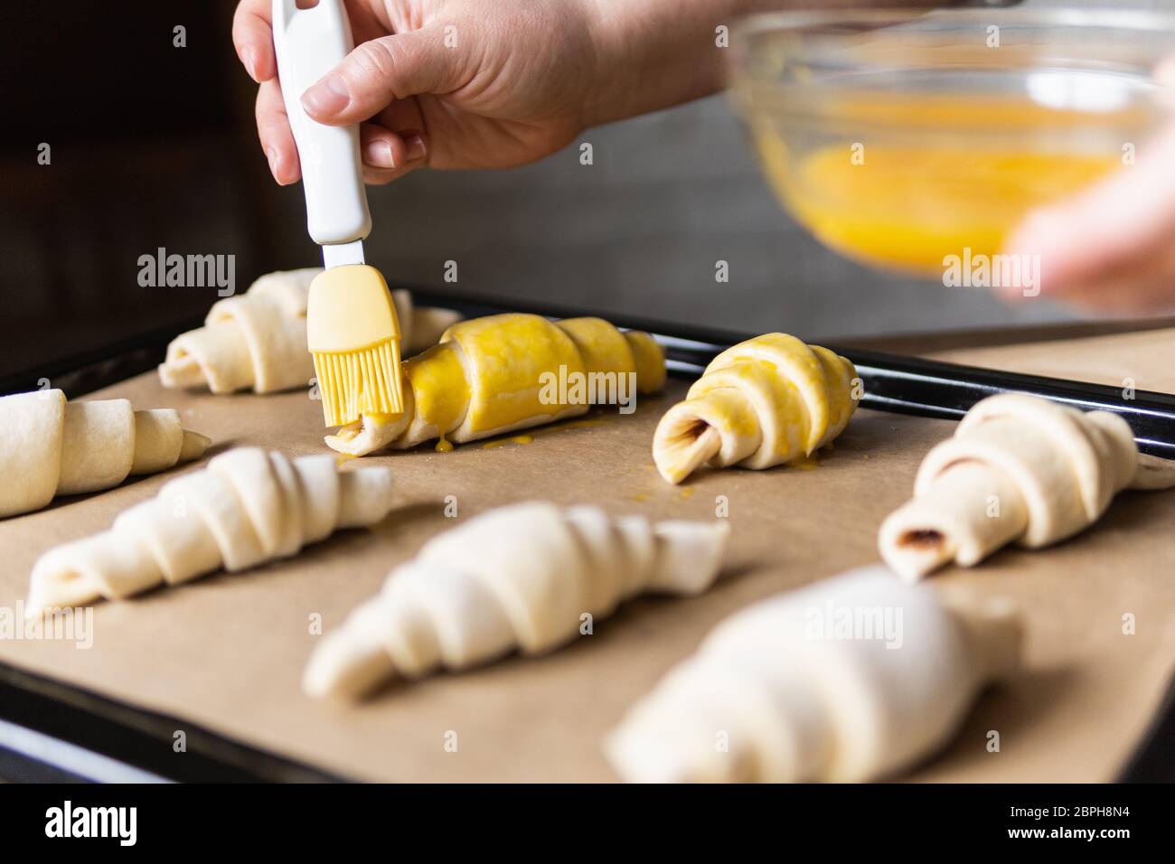 Baking croissants at home and covering the dough with egg yolk using