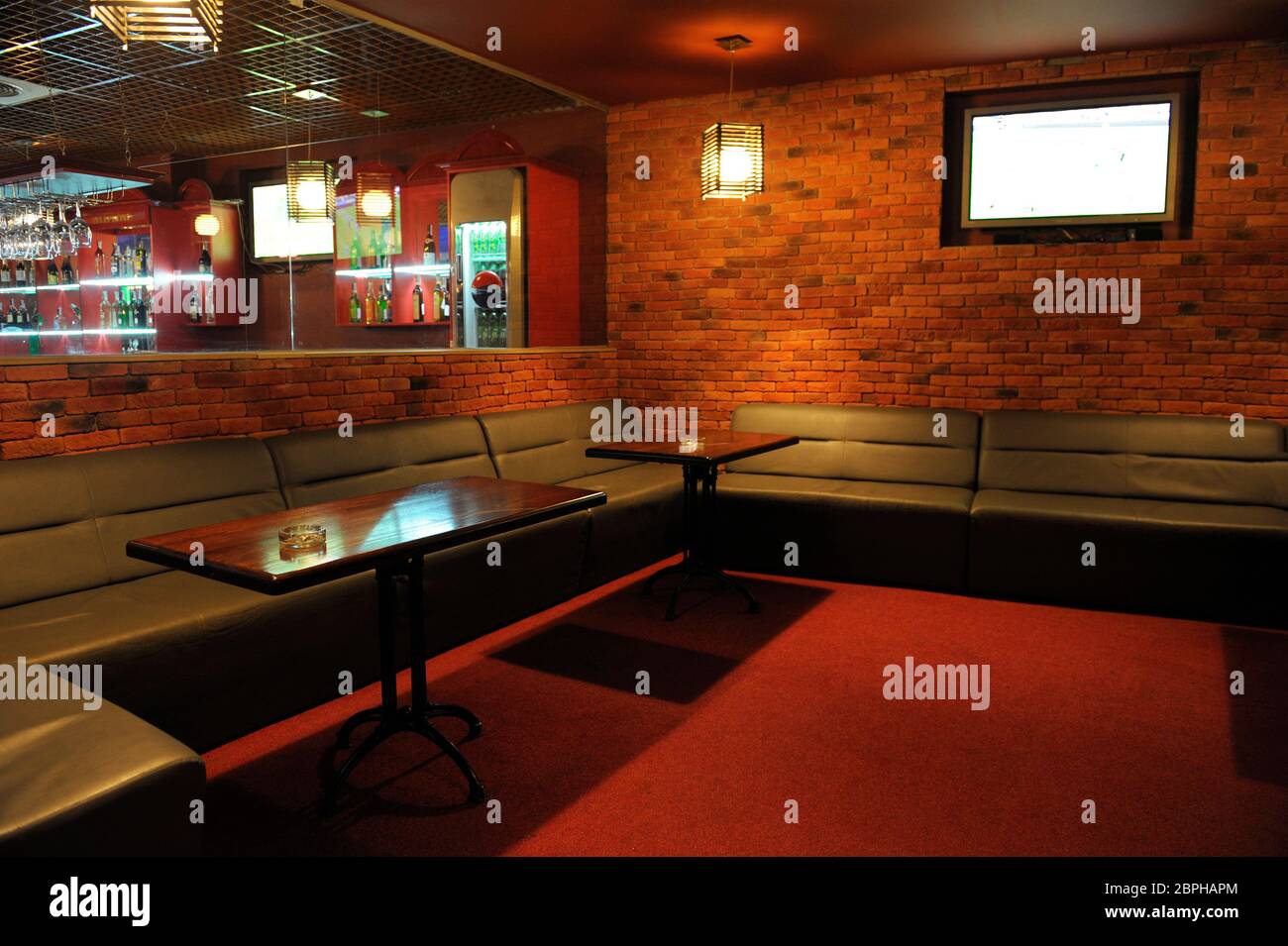Empty smoking room of a restaurant designed in red color brick walls,  couches and wooden tables with ashtrays Stock Photo - Alamy