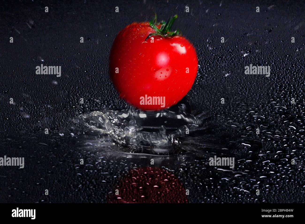 Fresh red Tomato falling in puddle of Water, with motion blure Stock Photo