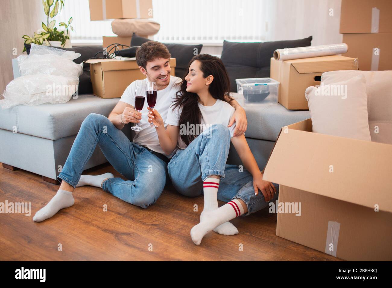 Young happy couple drinking wine, celebrating moving to new home and ...