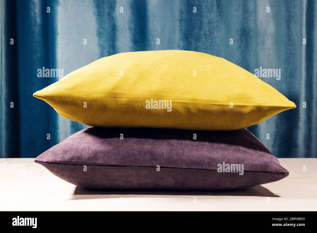 Yellow and purple pillows standing one on to another. Blue velvet background. Soft light coming from the top, Warm whitebalance Stock Photo