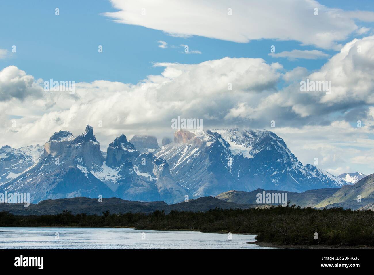 The jagged peaks of Cuernos del Paine, with a blue sky and white clouds above, beyond Lago Pehoe, Torres del Paine National Park, Patagonia, Chile Stock Photo