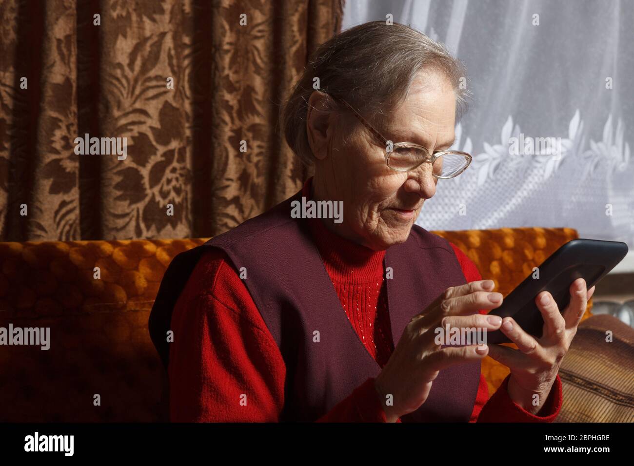 Very old woman reading e-book reader sitting in her sofa Stock Photo