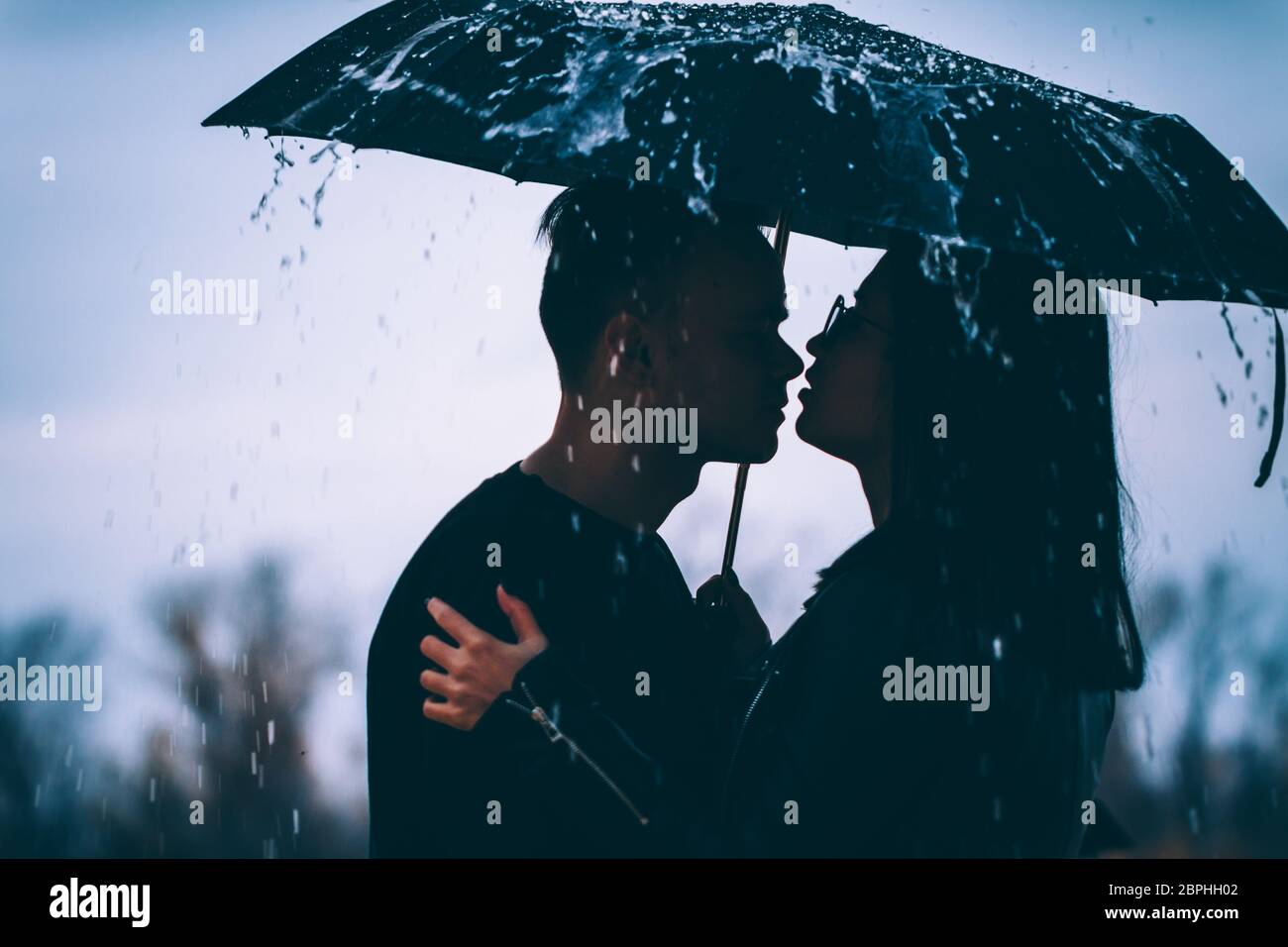 young couple standing under a dark umbrella Stock Photo - Alamy