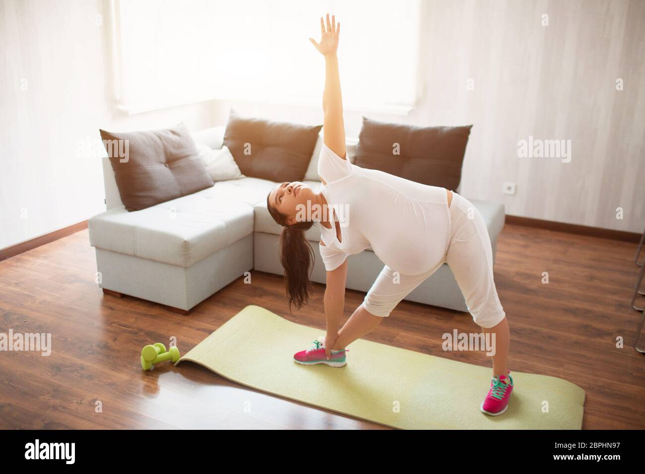 A pregnant woman works out on a yoga mat at home. Pregnancy and sports