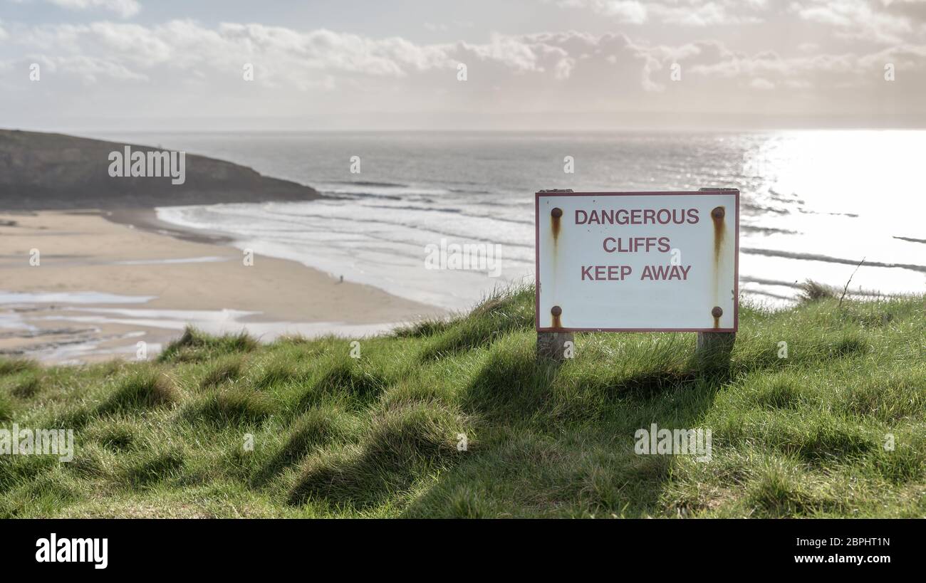 A sweeping beach on the South Wales coast, UK on a bright, winters day. There is a sign that says 'Dangerous Cliffs, keep away' Stock Photo