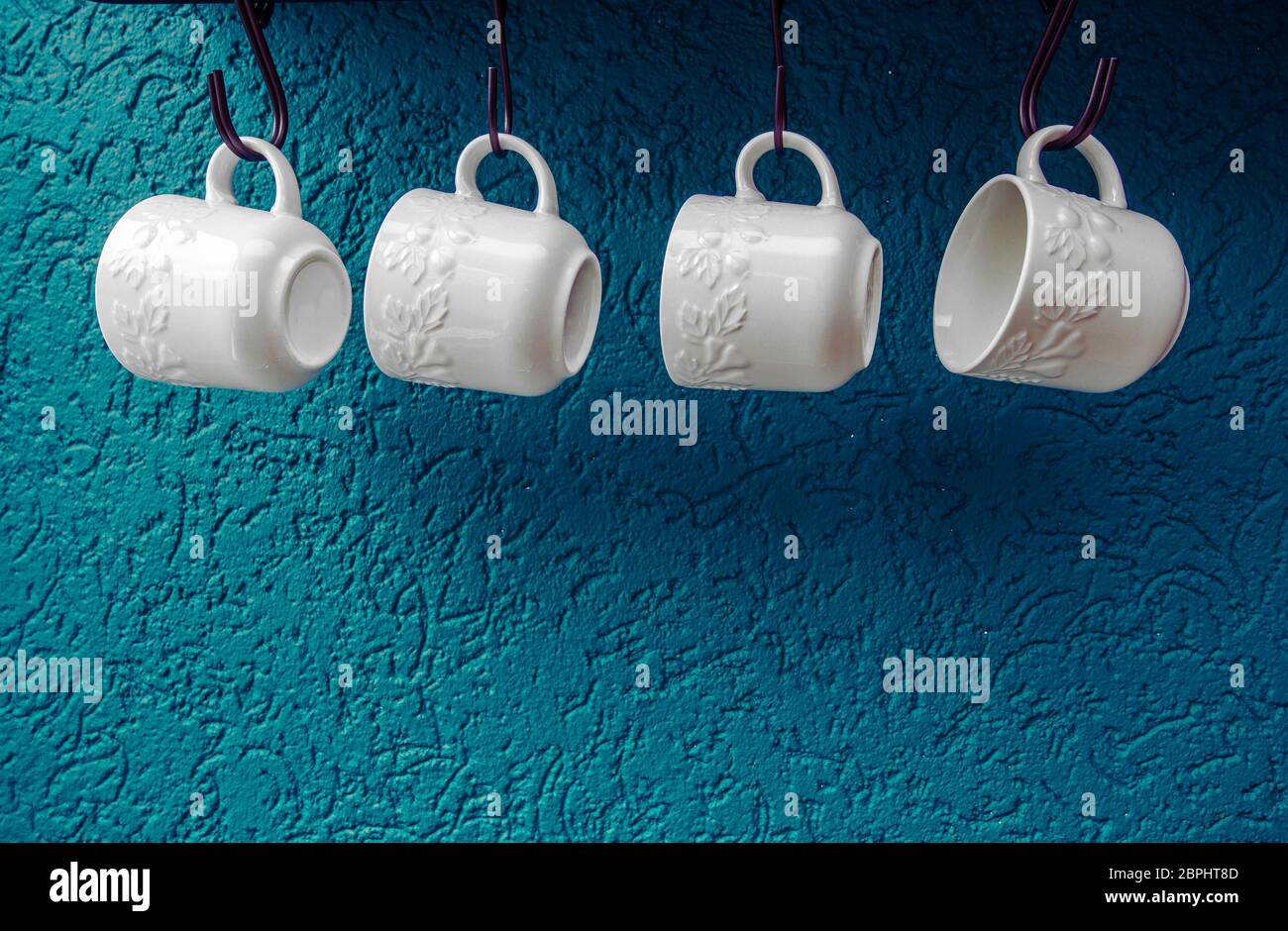 coffee cups hanging on hooks of blue kitchen wall modern interior design Stock Photo