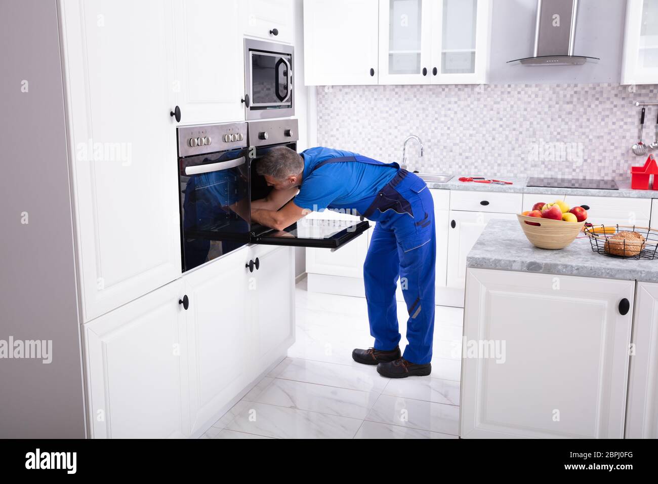 Mature Technician In Overall Repairing Oven In Kitchen Stock Photo