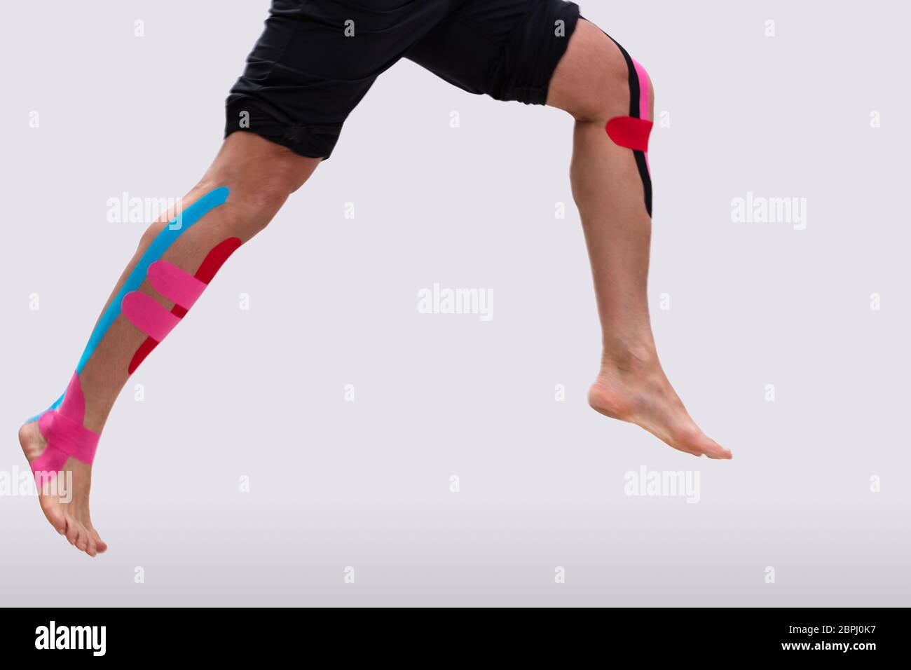 Low Section Of A Man Running With Physio Tape On His Legs Over White