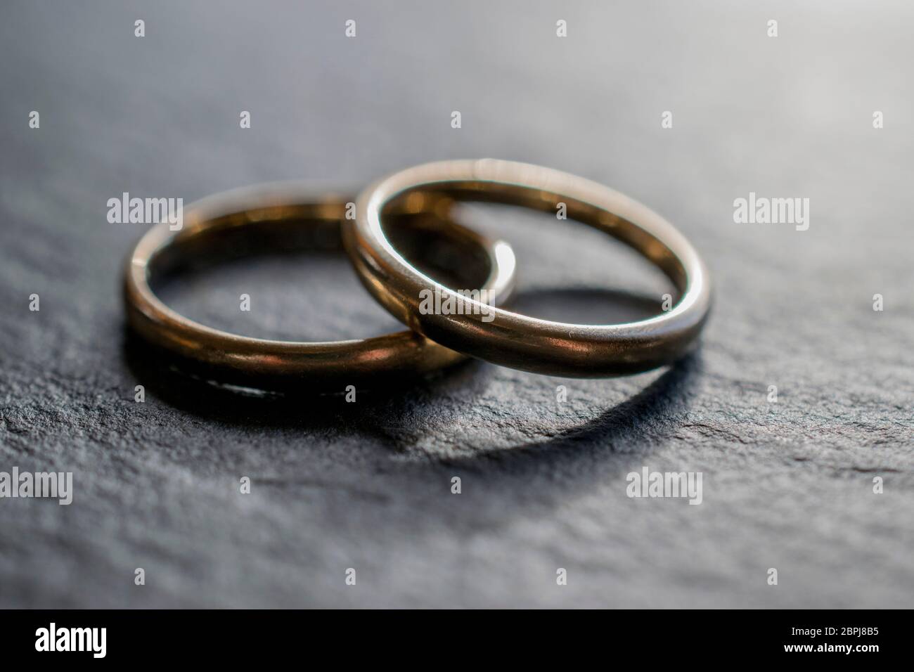 Two gold wedding bands overlapping on a slate tile Stock Photo