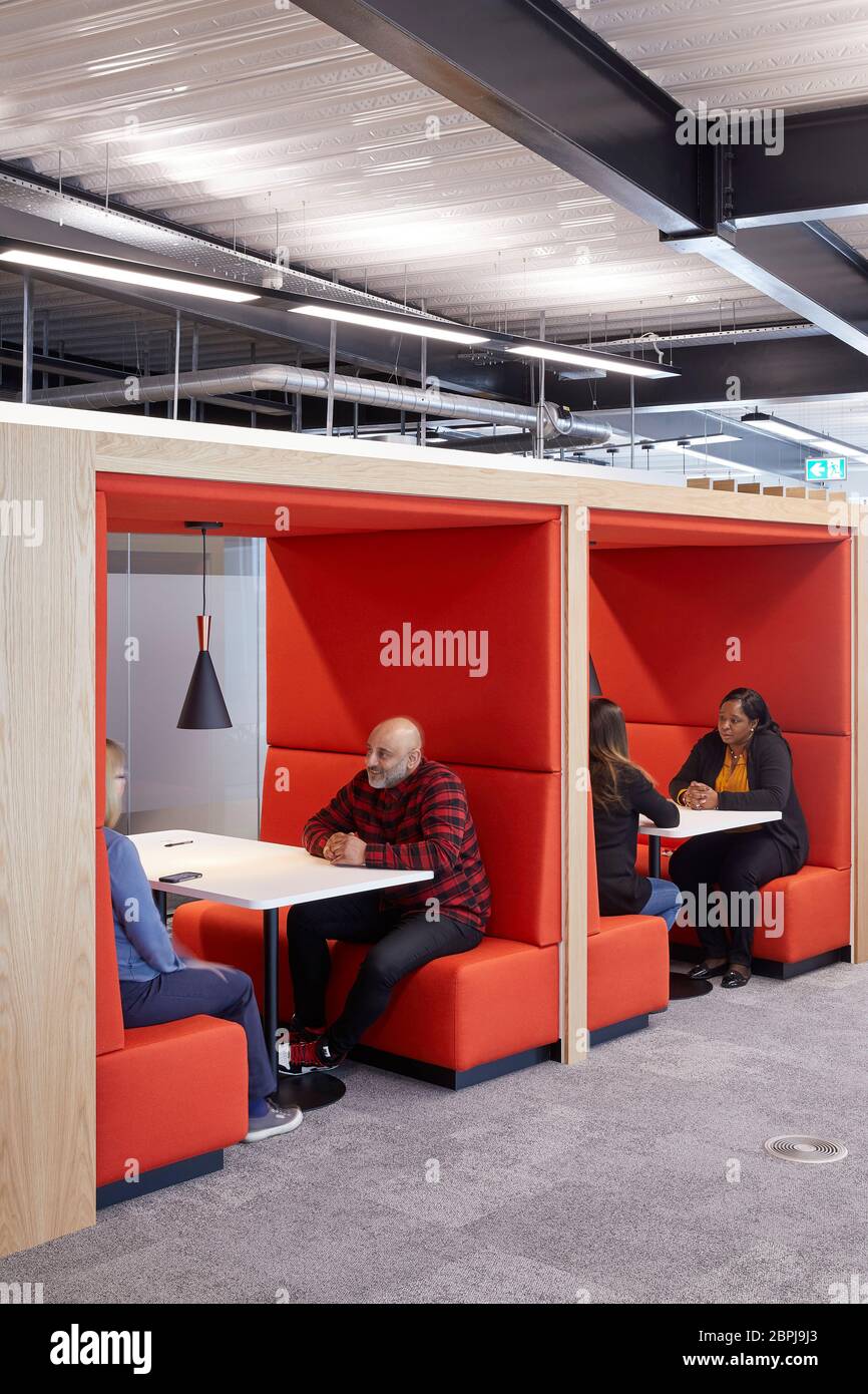 People seated in booths in a contemporary UK office interior with primary coloured furniture. UK