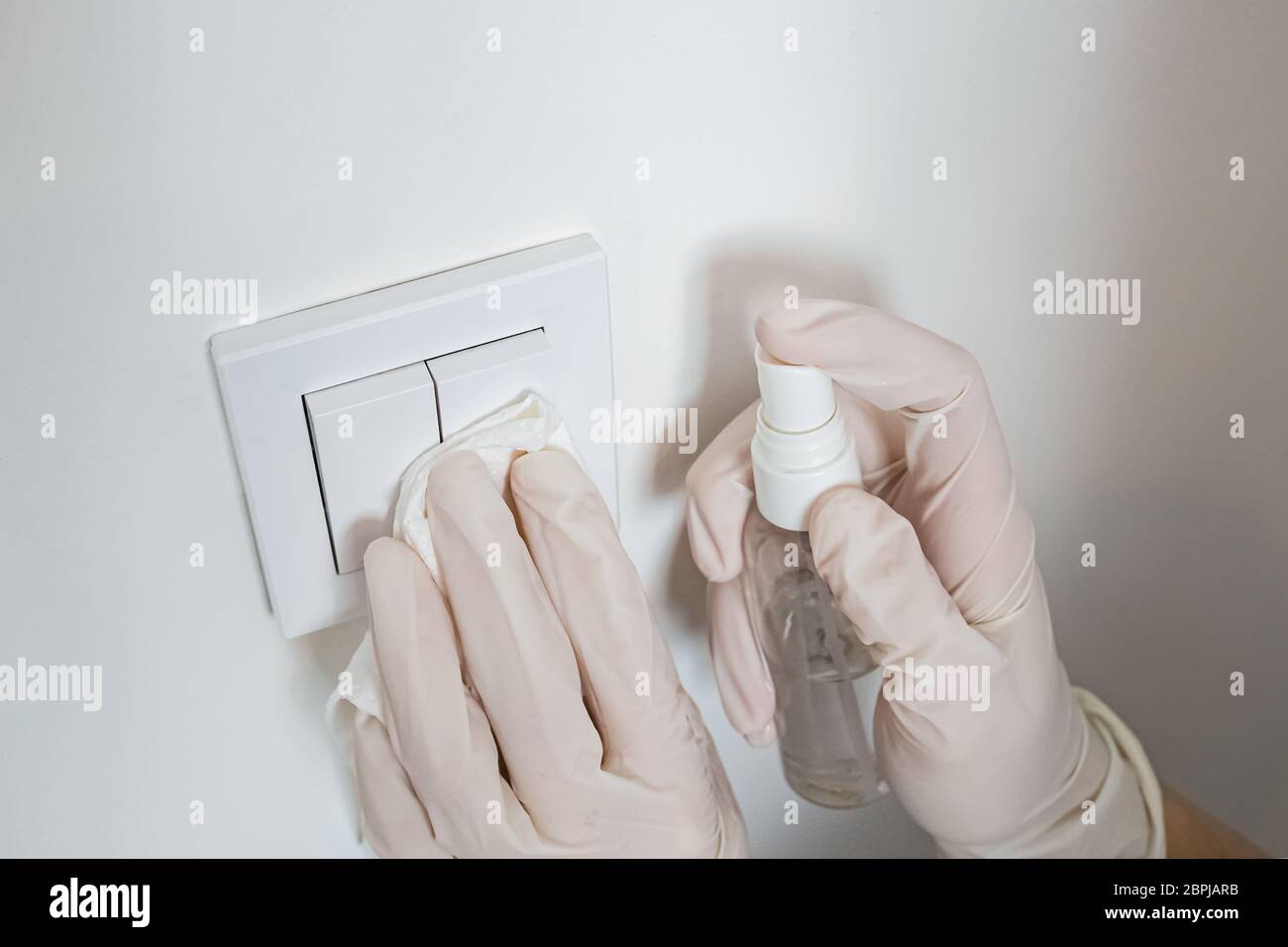 Woman wiping light switcher with antibacterial disinfecting spray Stock Photo