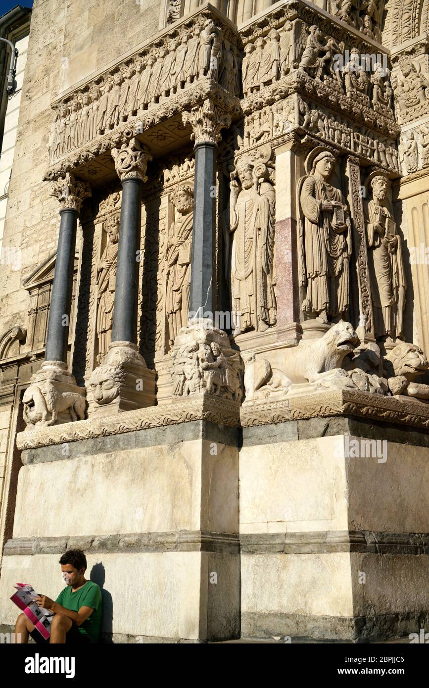 Romanesque sculptures decorated the portal of Church of St.Trophime with a visitor sitting underneath. Place de la Republique. Bouches-du-Rhone.France Stock Photo