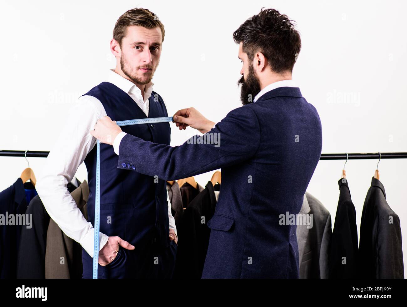 Businessman, client stand near hanger with suits while tailor working