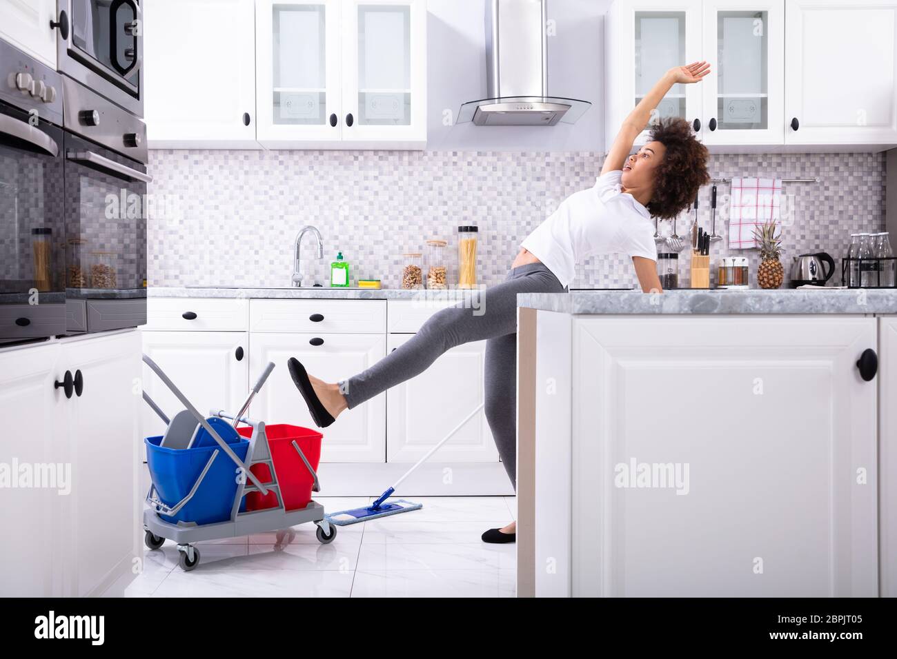 Close-up Of A Young African Woman Slipping While Mopping Floor In The Kitchen Stock Photo