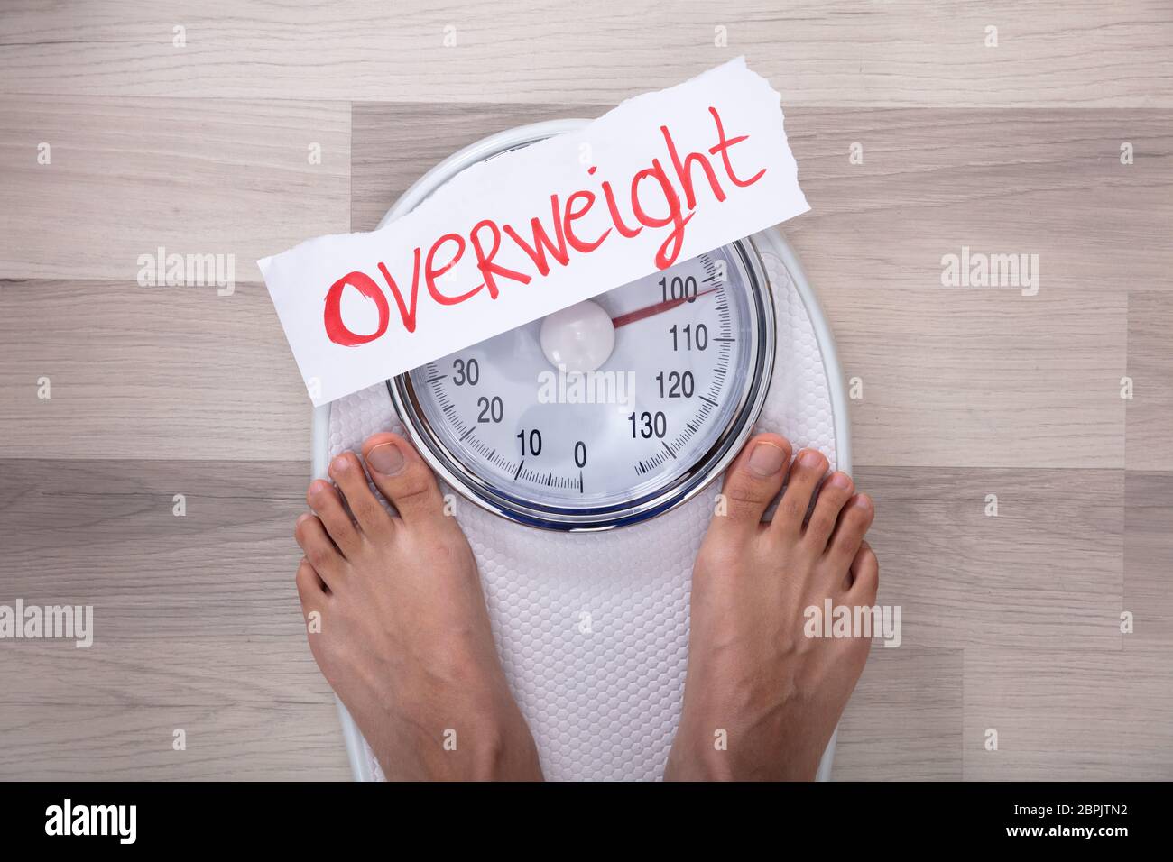 Close-up Of Woman's Feet On Weighing Scale Indicating Overweight On White Paper Stock Photo
