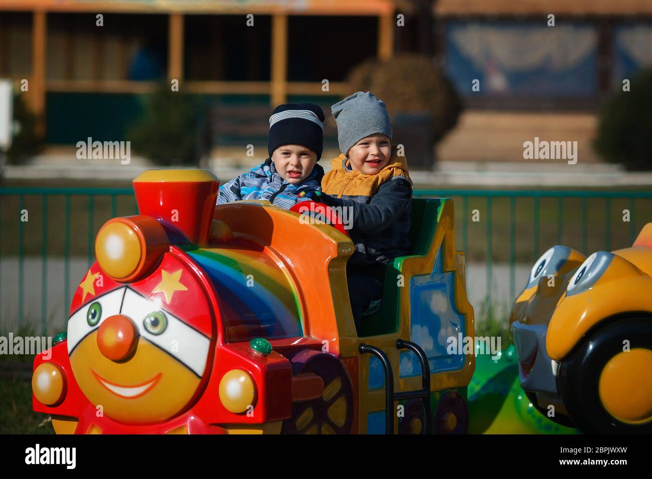 Children's rest in the amusement park. Two boys ride a children's colored locomotive by rail. Happy children on a walk on an autumn day. Stock Photo