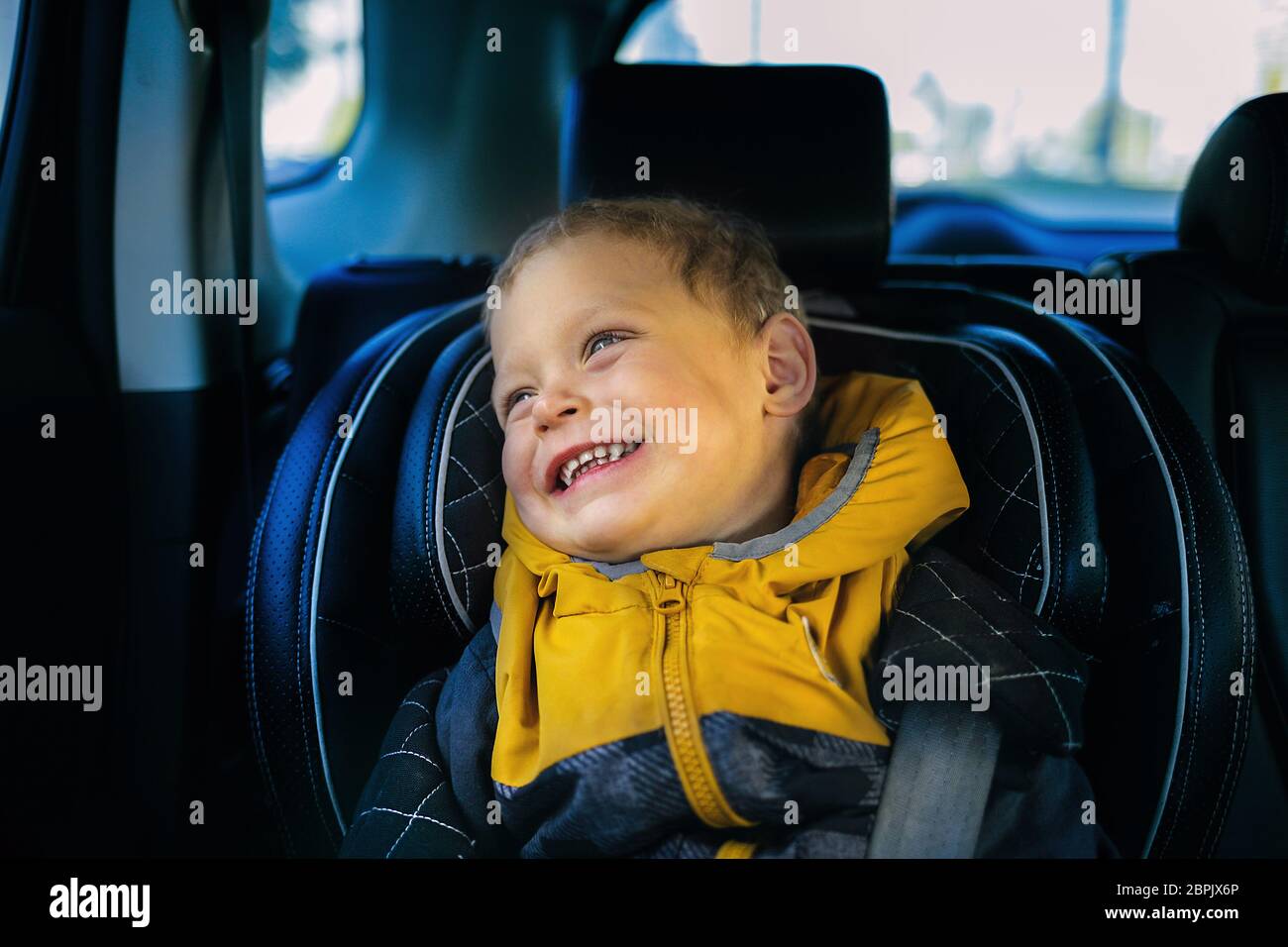 A joyful little boy smiles in a child's car seat. Child safety when