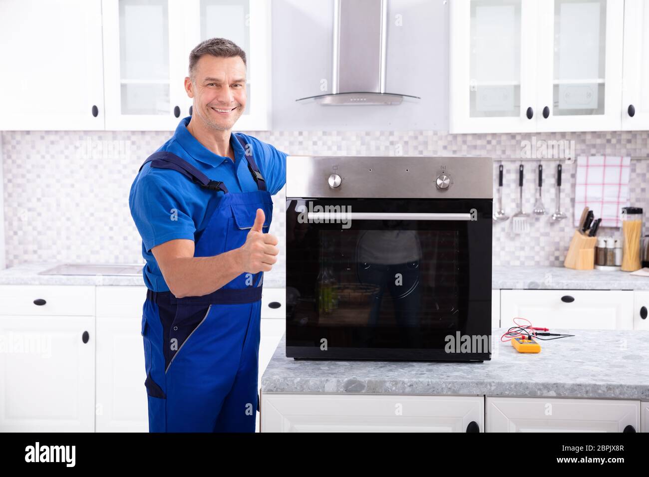 Mature Male Technician Repairing Oven On Kitchen Worktop Stock Photo