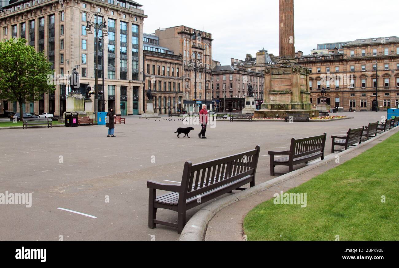 Only 2 people in Glasgow's George Square where there are normally thousands of visitors, tourists and Glaswegians passing through it. This empty, deserted square is like this because of the Covid-19, coronavirus pandemic that is rampaging through Britain and the country is in lockdown and a stay at home mode. May 2020. ALAN WYLI/EALAMY© Stock Photo