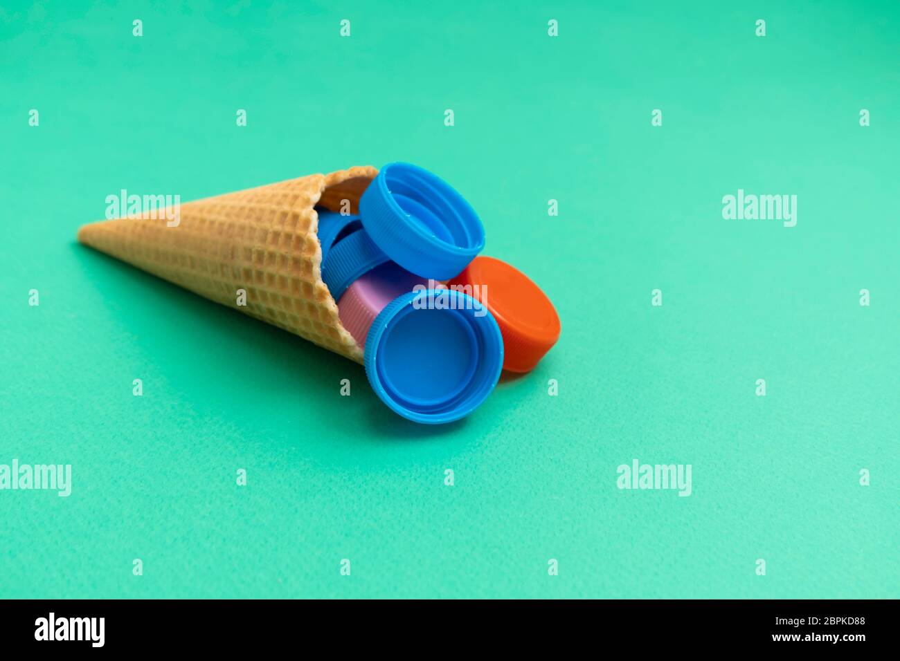 Plastic free and unnatural plastic food concept. Waffle cone with plastic bottle caps on green background Stock Photo