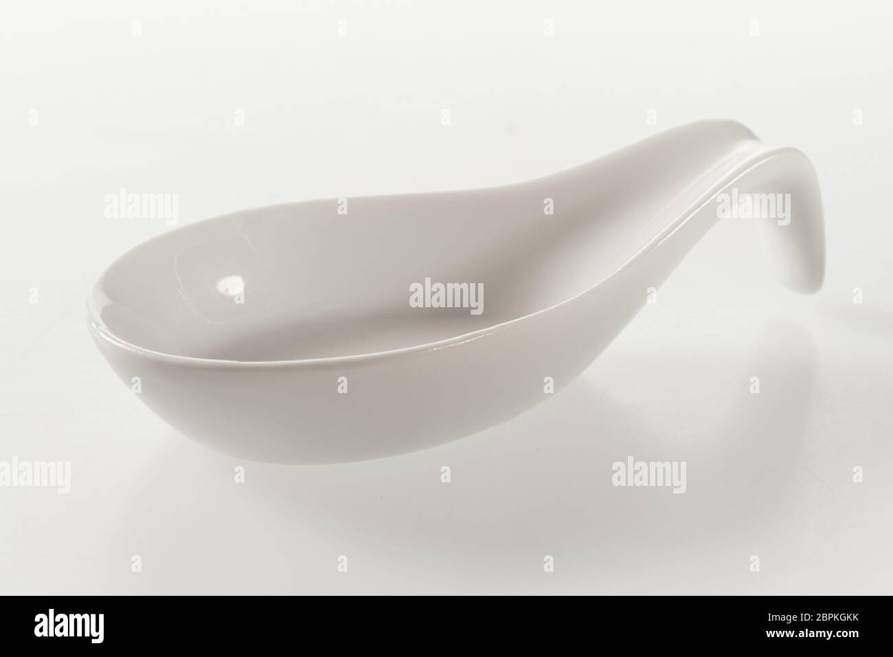 Clean empty white ceramic spoon for food presentation and styling diagonally on a white background with reflection Stock Photo
