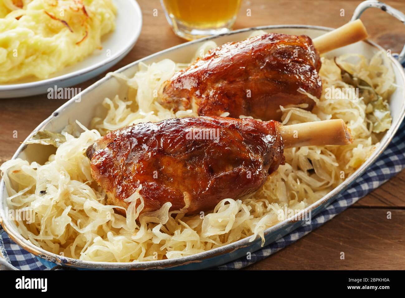 Marinated crispy pork hocks or eisbein on shredded cabbage in a rustic oval dish for traditional German cuisine Stock Photo