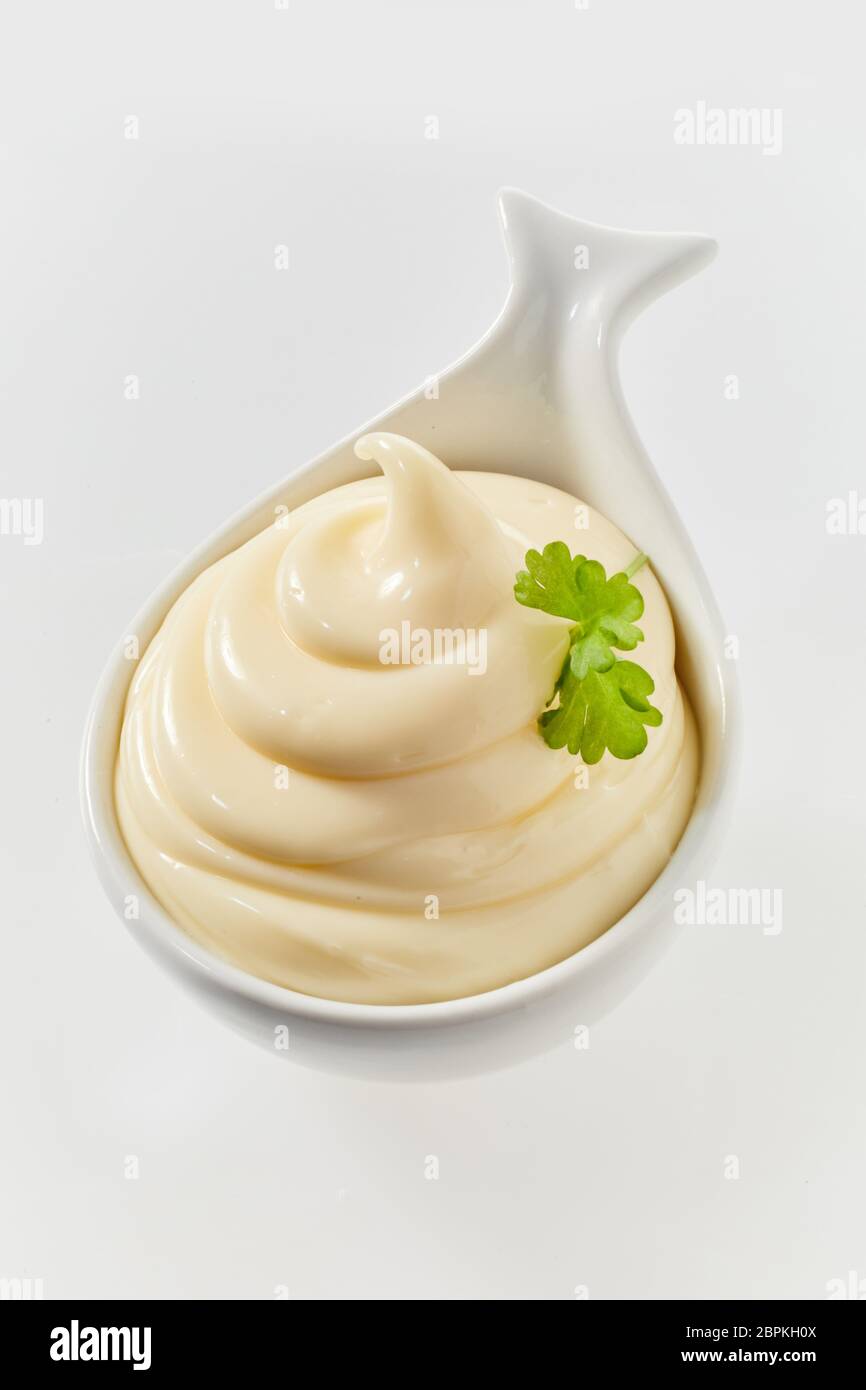 Twirled freshly made mayonnaise in a ceramic spoon to be served as an accompaniment to a formal meal high angle on white Stock Photo
