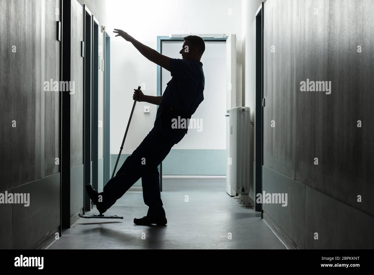 Silhouette Of A Mature Man Falling While Mopping Floor In The Corridor Stock Photo