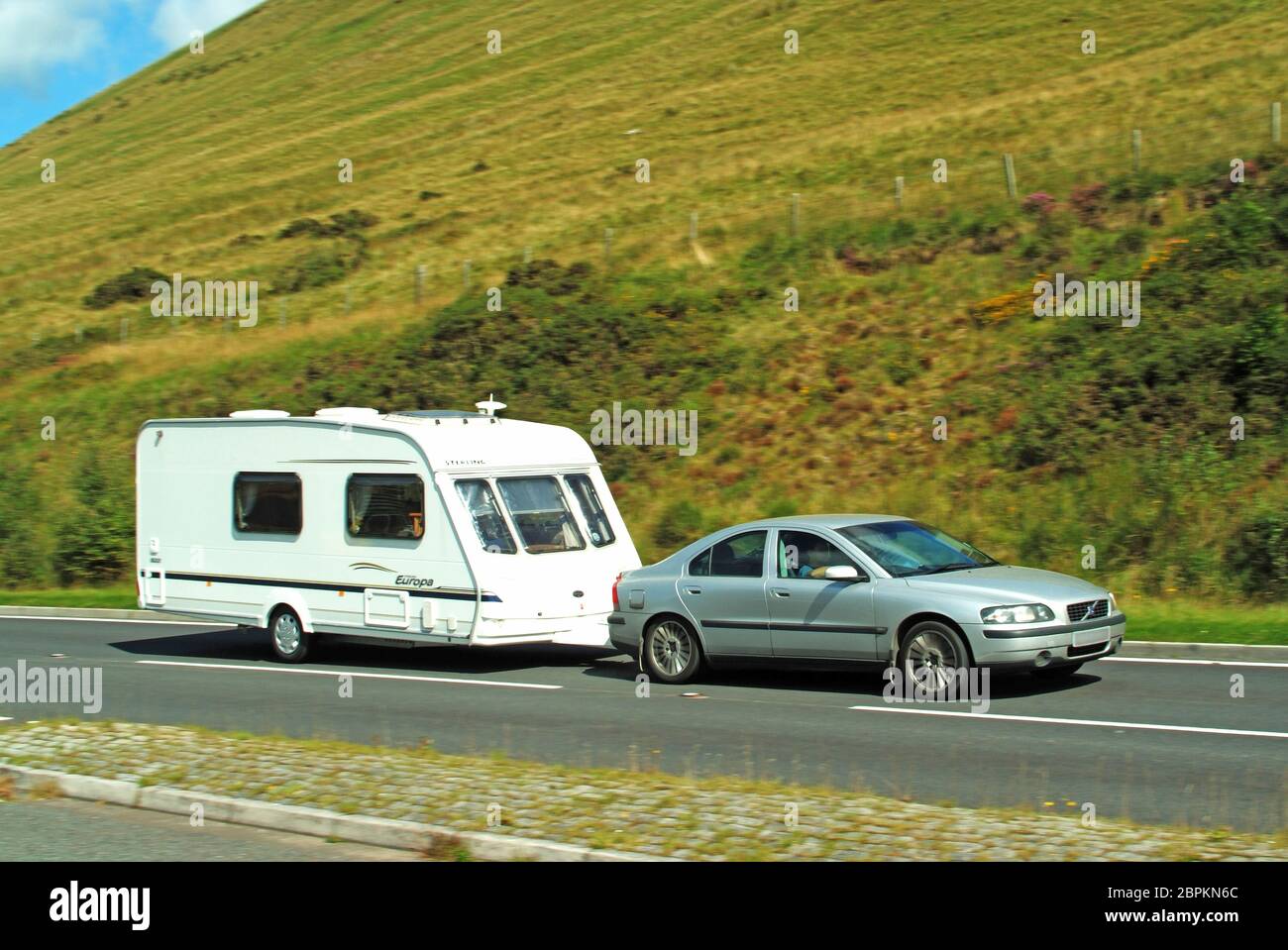 Side view of man driving car towing white caravan on rural scenic countryside road in the Brecon Beacons National Park Powys South Wales UK Stock Photo