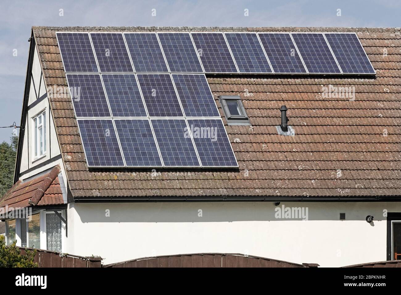 Solar Panels in sunshine installed on south facing roof on sunny blue sky day detached house alongside an existing roof light panel Essex England UK Stock Photo