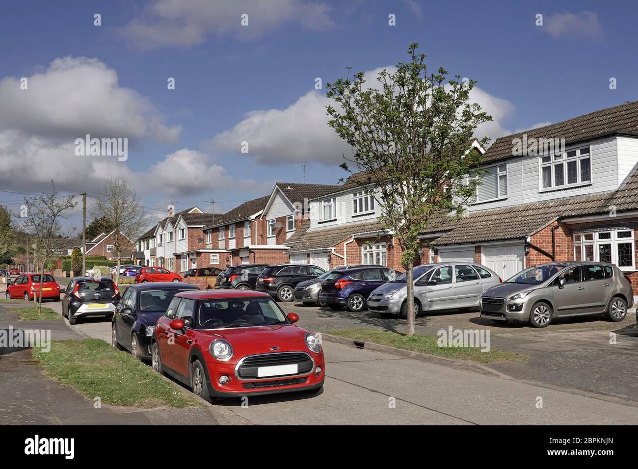 Residential suburb street car parking scene in road & houses with cars on original lawn front garden now paved vehicle park space  Essex England UK Stock Photo