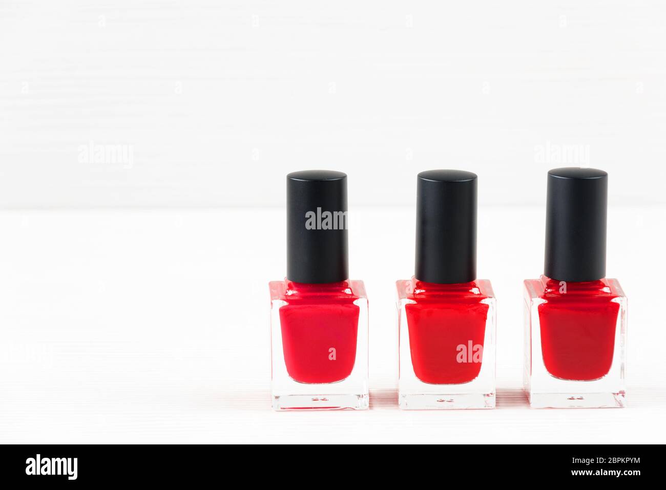 Close-up image of three Red nail polish bottles on white wooden background. Stock Photo