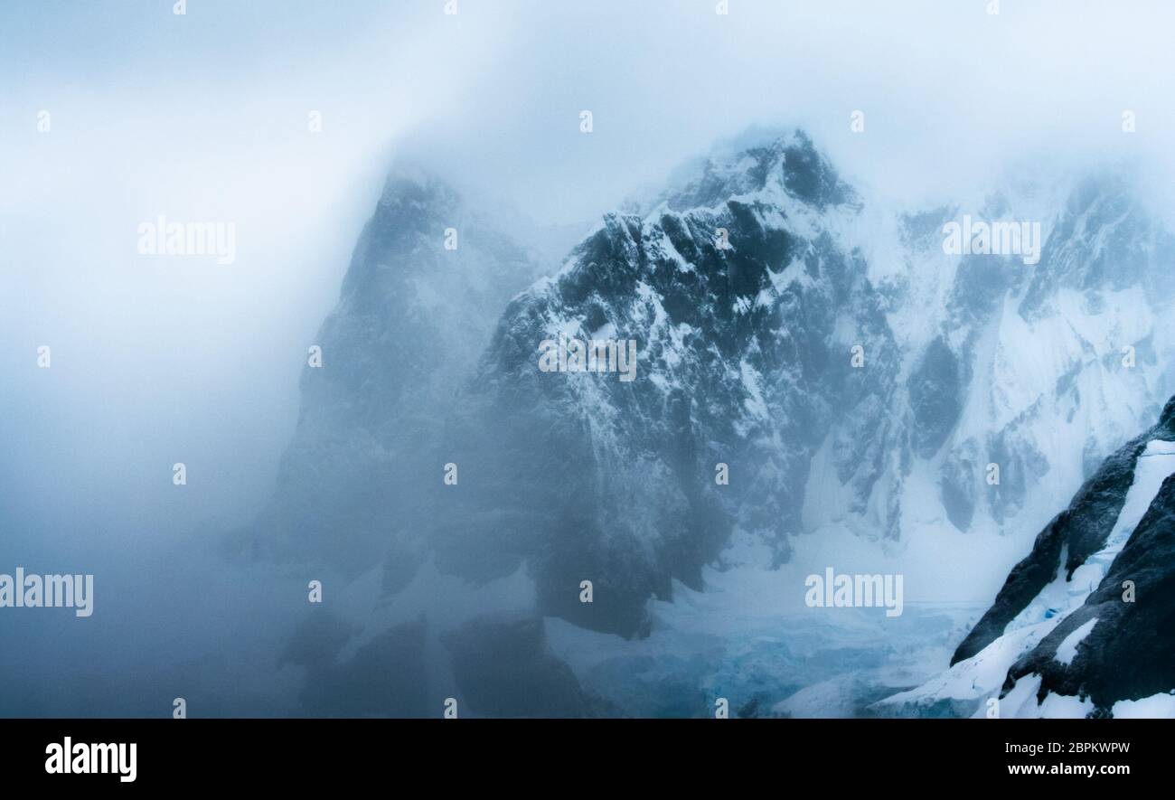 Inclement weather with mist, rain, and snow enshrouding jagged rocky volcanic landscape in the Antarctic Peninsula Stock Photo